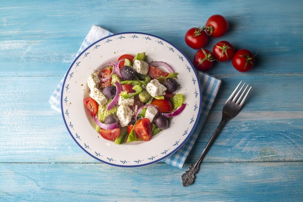 Easy Red White and Blue Salad Recipe for Your BBQ 7 A plate of red white and blue salad with tomatoes, feta cheese, Kalamata olives, cucumbers, and red onions on a blue wooden table