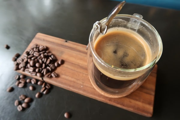 How Much Caffeine in Decaf Espresso: Brewing Insights 7 A glass cup of decaf espresso with crema on top, served on a wooden board beside scattered coffee beans