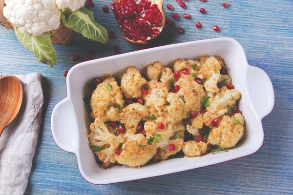 Cauliflower Bake: Deliciously Cheesy and Healthy Recipe 7 A baked cauliflower dish topped with breadcrumbs, fresh parsley, and pomegranate seeds, served in a white dish with a pomegranate and cauliflower