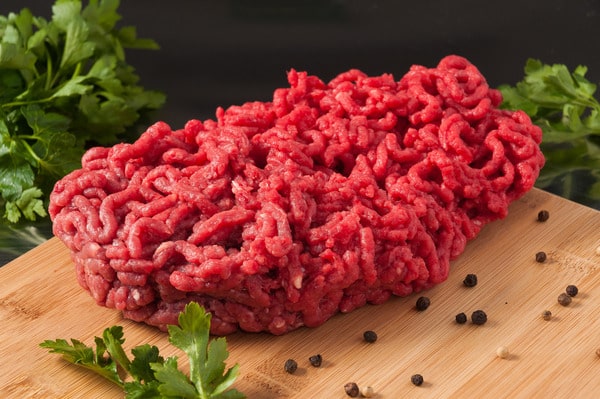 Calories in Ground Beef: Health Facts You Should Know 8 A neatly shaped portion of raw ground beef rests on a wooden cutting board, surrounded by parsley and scattered peppercorns