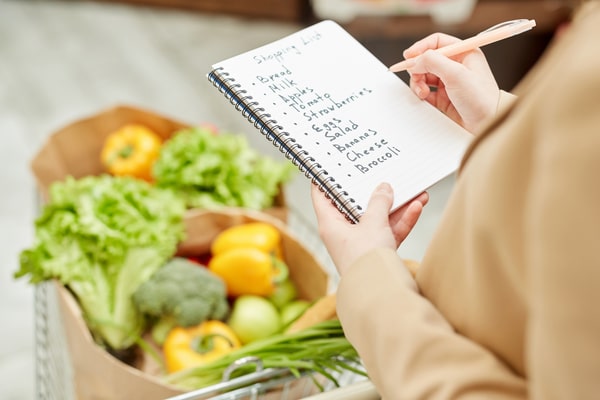 Keto Meal Prep Guide: 19 Quick Ideas and Time-Saving Hacks 8 A person holding a shopping list while standing by a grocery cart filled with fresh vegetables