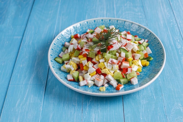 Easy Red White and Blue Salad Recipe for Your BBQ 8 A blue plate of red white and blue salad made with crab sticks, cucumbers, corn, eggs, and garnished with fresh dill