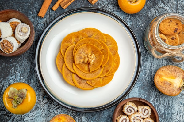 Keto Pumpkin Cookies: Perfect for Holiday Baking Ideas 8 A decorative plate of sliced pumpkin pancakes arranged in a flower pattern, surrounded by cookies, cinnamon sticks, and fresh persimmons
