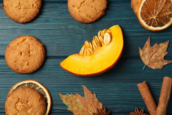 Keto Pumpkin Cookies: Perfect for Holiday Baking Ideas 9 Round keto pumpkin cookies arranged with a fresh pumpkin slice, dried oranges, cinnamon sticks, and autumn leaves on a blue wooden background