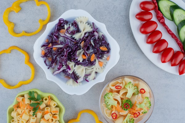 Easy Red White and Blue Salad Recipe for Your BBQ 10 A white bowl of red white and blue salad with farfalle pasta, purple cabbage, and carrots, served alongside fresh vegetables and pasta dishes