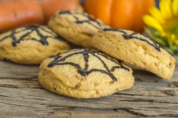 Keto Pumpkin Cookies: Perfect for Holiday Baking Ideas 10 Close-up of keto pumpkin cookies decorated with chocolate spiderweb designs, placed on rustic wooden surface with pumpkins in the background