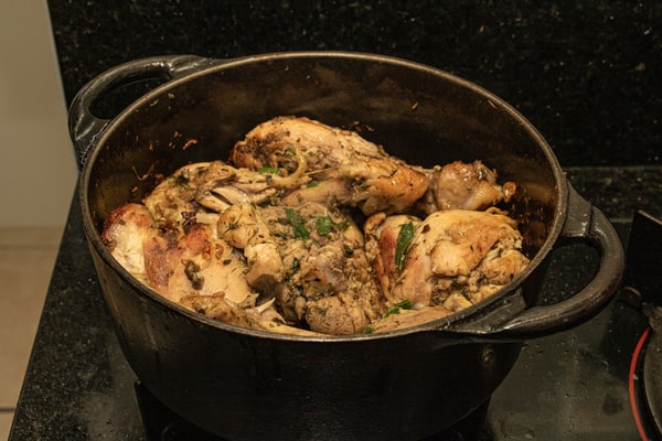 13 Keto Crockpot Chicken Recipes for Effortless Cooking 7 A close-up, high-angle view shows seasoned and browned chicken pieces cooking in a heavy black cast iron pot on a stove top with a dark counter in the background.