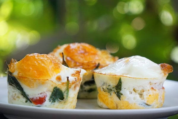 Keto Egg Cups: A Quick Breakfast Solution 4 Keto egg cups with melted cheese, spinach, and vegetables served on a white plate