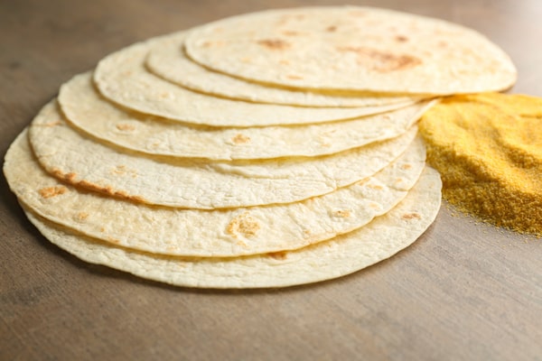 Are Corn Tortillas Keto or Just a Carb Trap? 5 A stack of corn tortillas placed on a wooden surface beside a small pile of cornmeal