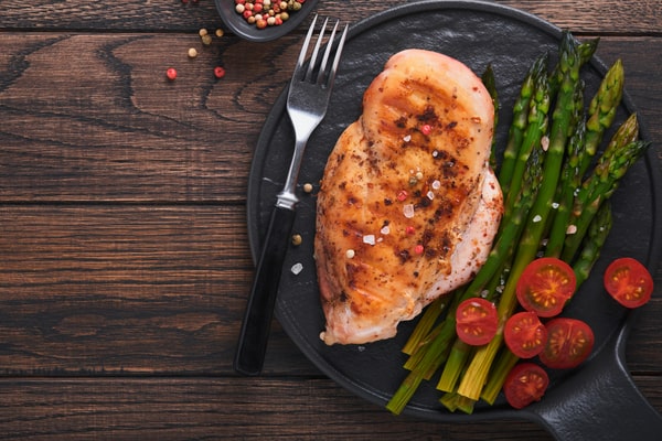 Pan Seared Chicken Breast Made Easy in Just Minutes 8 Pan-seared chicken breast served with asparagus and sliced cherry tomatoes on a black plate