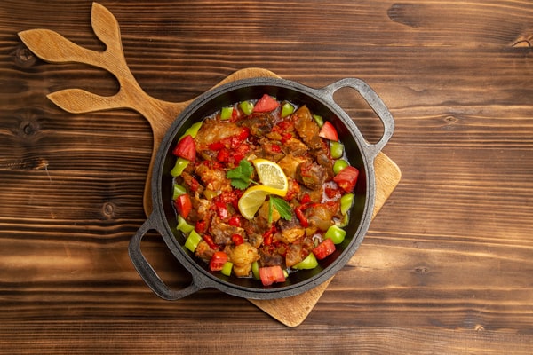 Keto Turkey Chili With Big Flavor Boost 8 A skillet of keto turkey chili with bell peppers, tomatoes, and lemon garnish, served on a wooden board over a rustic brown table
