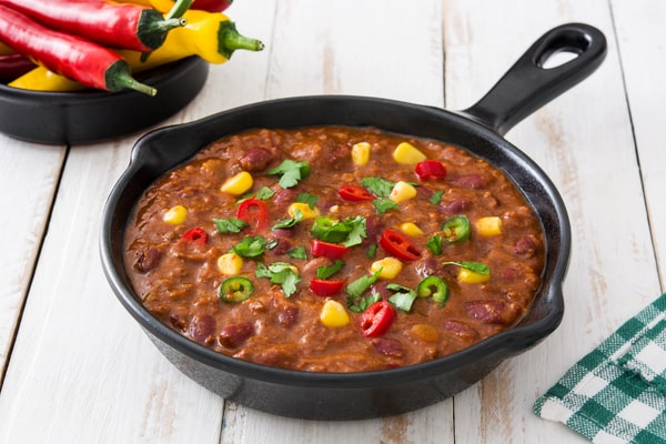 Keto Turkey Chili With Big Flavor Boost 9 A skillet of keto turkey chili topped with sliced chili peppers, corn, and fresh cilantro, set on a white wooden table