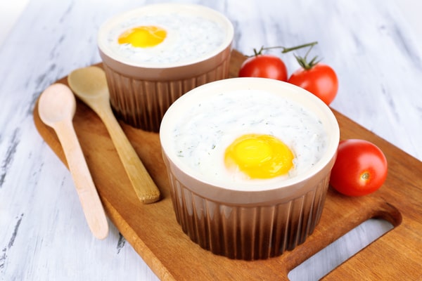 Keto Egg Cups: A Quick Breakfast Solution 10 Keto egg cups with creamy egg and herb mixture topped with yolk served in brown ramekins beside fresh cherry tomatoes