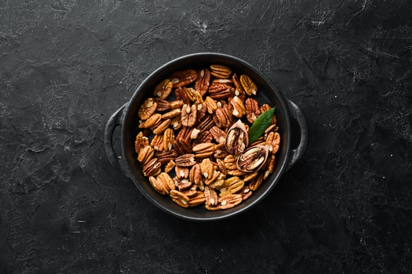 A black bowl filled with keto candied pecans, some glazed and garnished with a green leaf