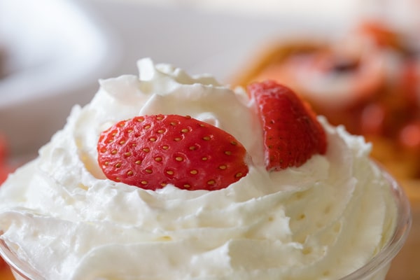 Is Cool Whip Low Carb? A Guide for Low-Carb Dieters 5 A close-up, shallow-depth-of-field shot shows a mound of fluffy whipped cream topped with two pieces of bright red strawberry.