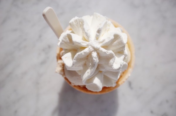 Is Cool Whip Low Carb? A Guide for Low-Carb Dieters 3 An overhead close-up shows a large star-piped swirl of whipped cream in a small waffle cone cup with a white plastic spoon resting inside on a bright, marble surface.