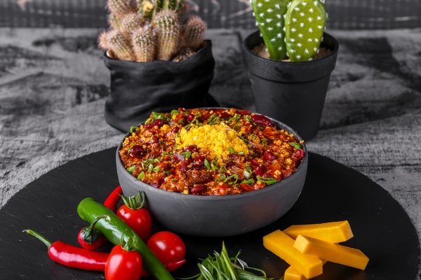 Keto Turkey Chili With Big Flavor Boost 2 A bowl of keto turkey chili topped with cheese and herbs, surrounded by fresh peppers, tomatoes, and cheddar slices