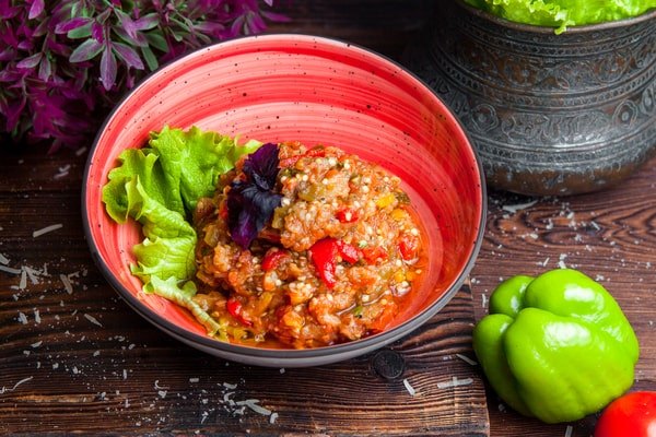 Keto Turkey Chili With Big Flavor Boost 4 A bowl of keto turkey chili with red peppers and herbs, served on lettuce leaves in a red dish beside fresh green bell pepper