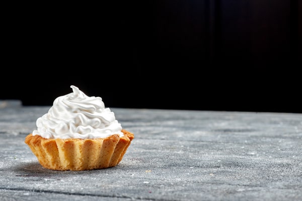 Is Cool Whip Low Carb? A Guide for Low-Carb Dieters 2 A single small, fluted pastry tart filled with a generous swirl of white whipped cream sits on a speckled grey surface against a black background.