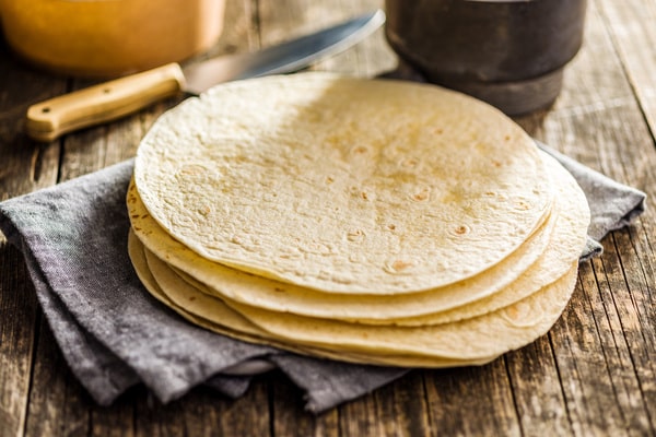 A stack of tortillas on a cloth napkin resting on a wooden table