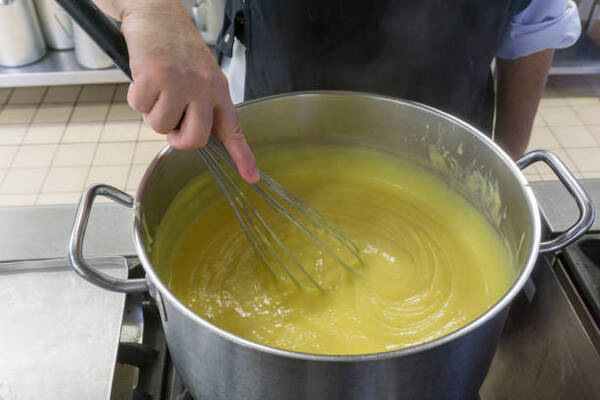 A woman whisking custard in a saucepan over stovetop